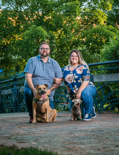 cody and stephanie ward, owners of the homeowners helper llc, kneeling with their dogs at a park in frederick md