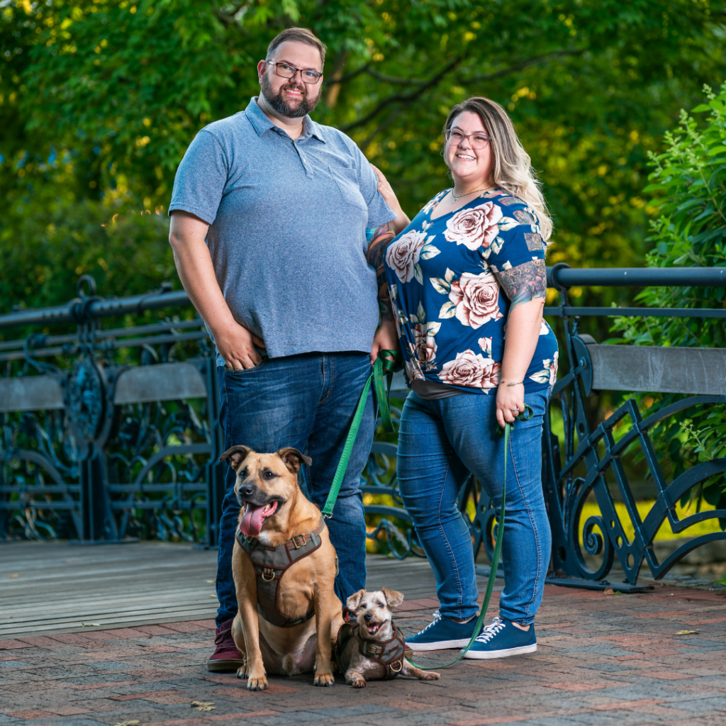 Cody and Stephanie ward, owners of The Homeowners Helper LLC - Frederick general contractors. They are posing with their dogs, at a park on a summer day in Frederick MD