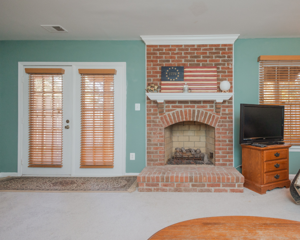 View of the brick fireplace and french patio doors in a modern country basement remodel project by the Homeowners Helper