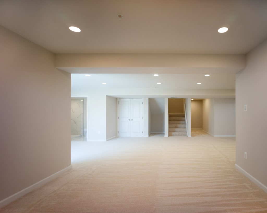 Another view of a basement remodeling project with cream colored wall-to-wall, neutral cream walls, and recessed lighting.