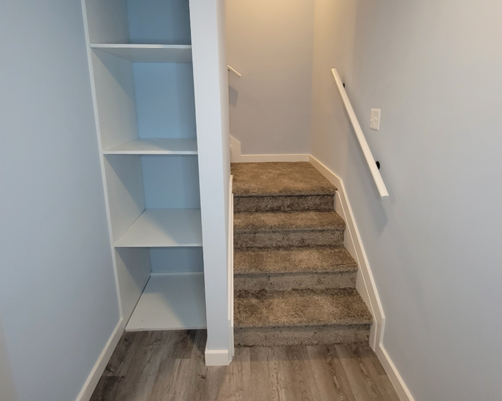 A split basement staircase next to built in shelving from a basement project