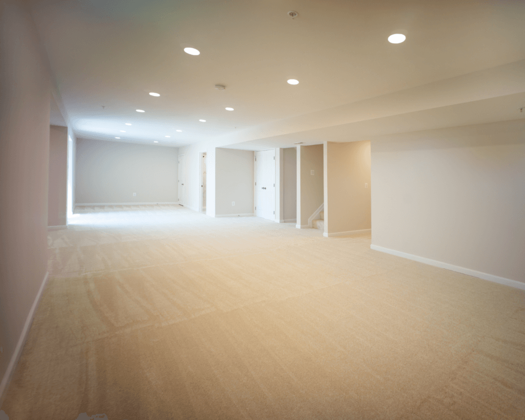A basement remodeling project with cream colored wall-to-wall, neutral cream walls, and recessed lighting.