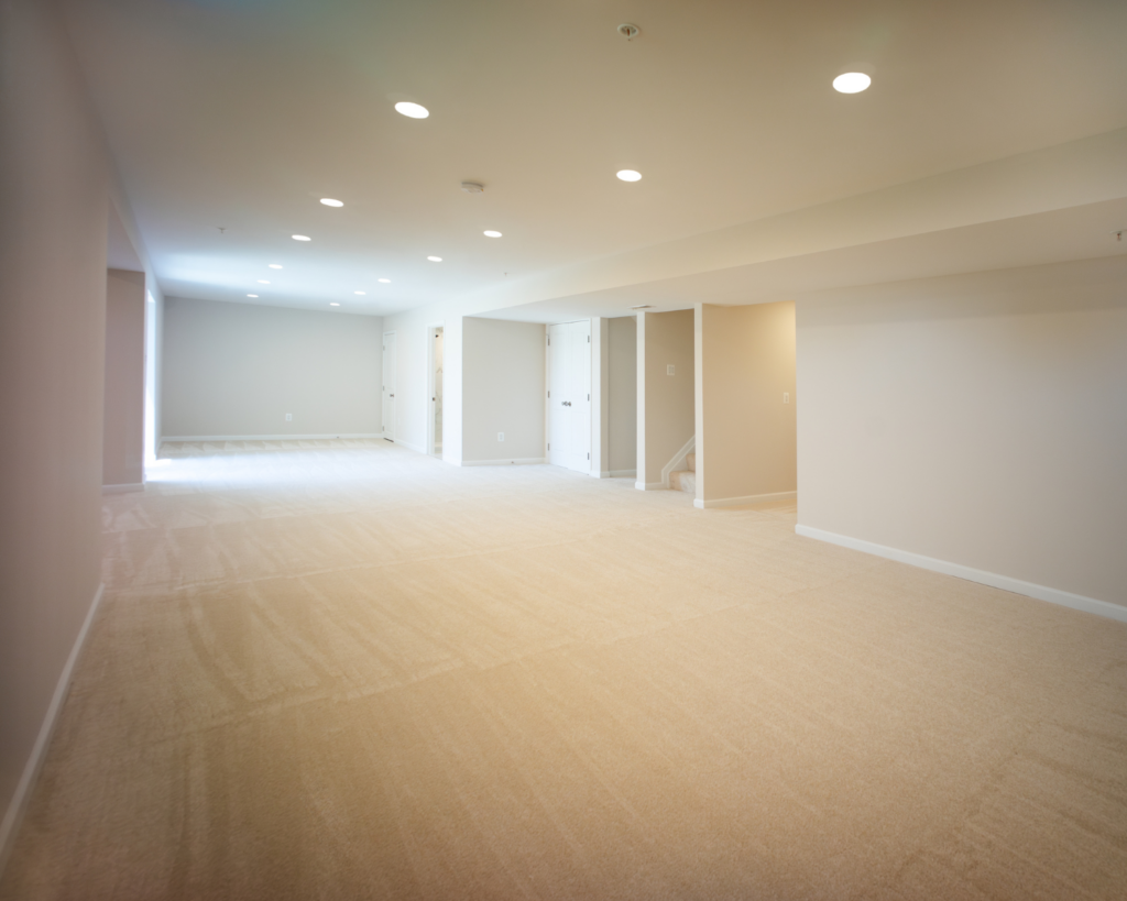 A basement remodeling project with cream colored wall-to-wall, neutral cream walls, and recessed lighting.